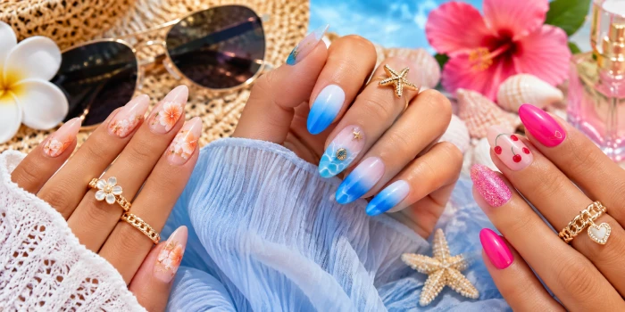 A close-up of manicured hands featuring simple cute summer nails in floral peach, blue ombre, hot pink, cherry, and glitter designs with tropical flowers, seashells, sunglasses, and beach-inspired accessories.