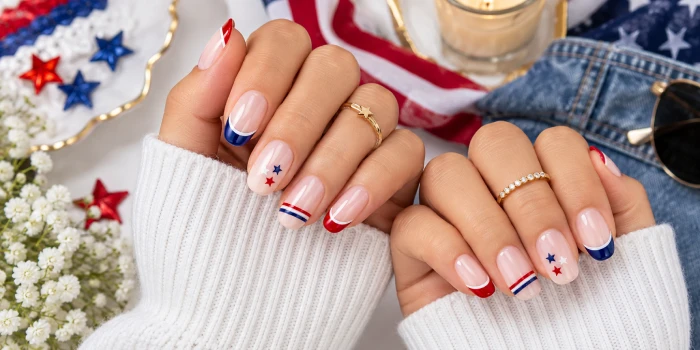 Minimalist patriotic nails for a clean girl look featuring glossy nude nails with subtle red, white, and navy French tips, tiny stars, and elegant gold rings.