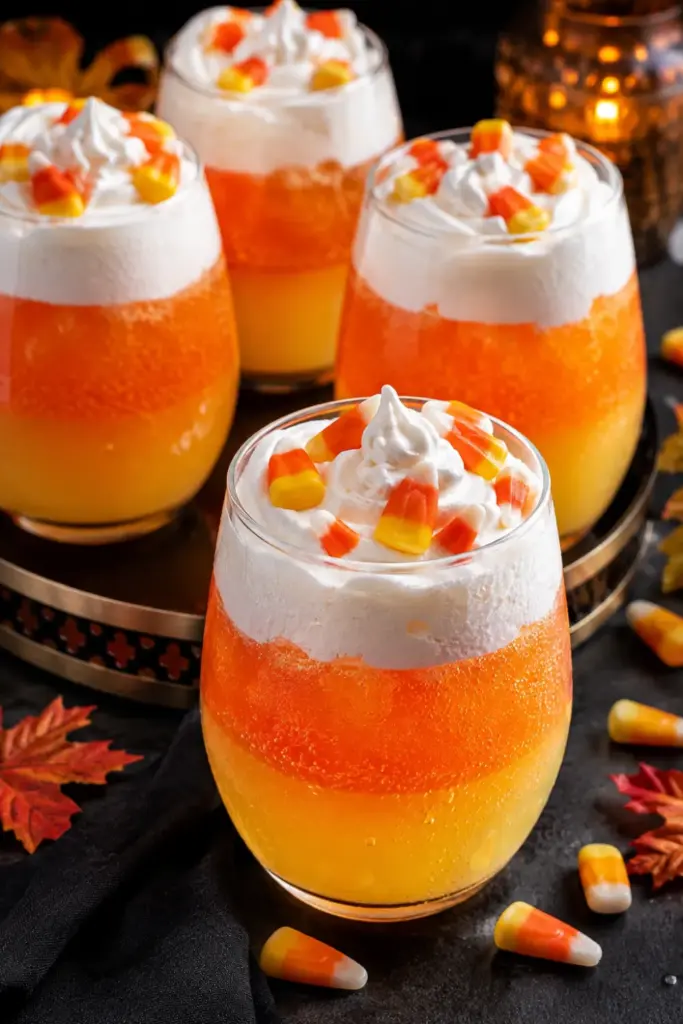 Candy Corn Halloween Punch made with pineapple juice, orange soda, vodka, whipped topping, and candy corn in a colorful layered Halloween presentation.