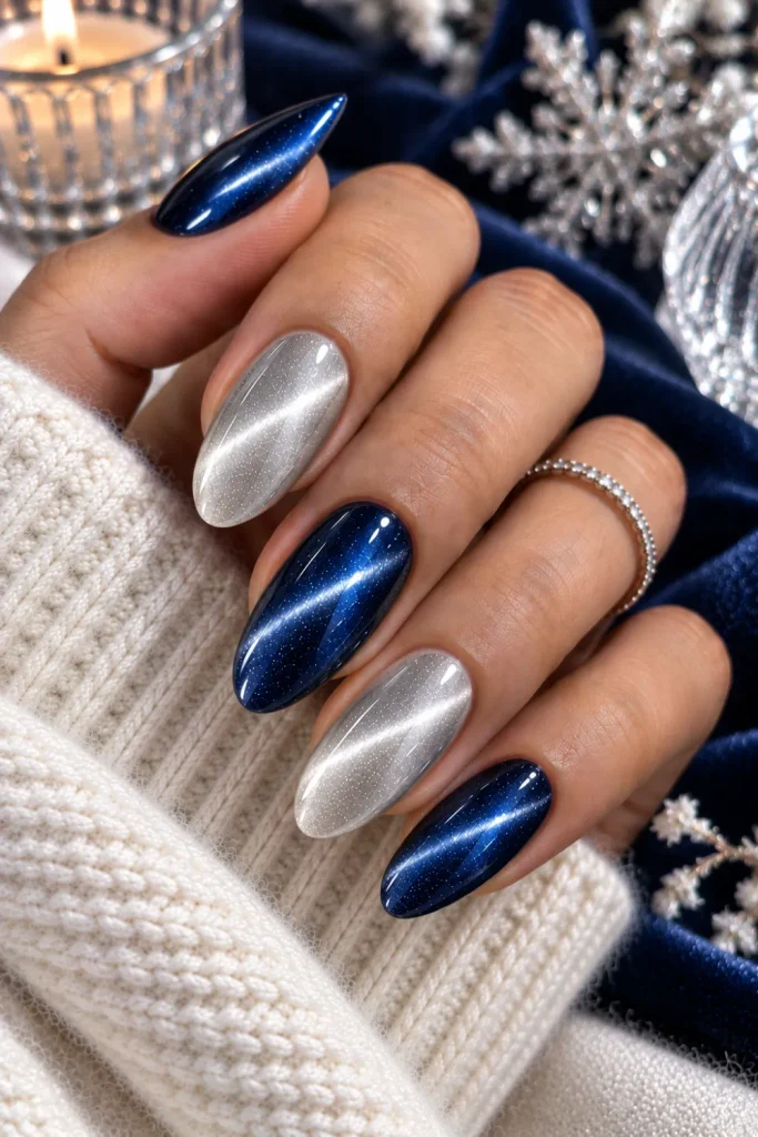 Silver and navy cat-eye winter nails with icy magnetic contrast, glossy almond shape, luminous metallic accents, and modern luxe styling.