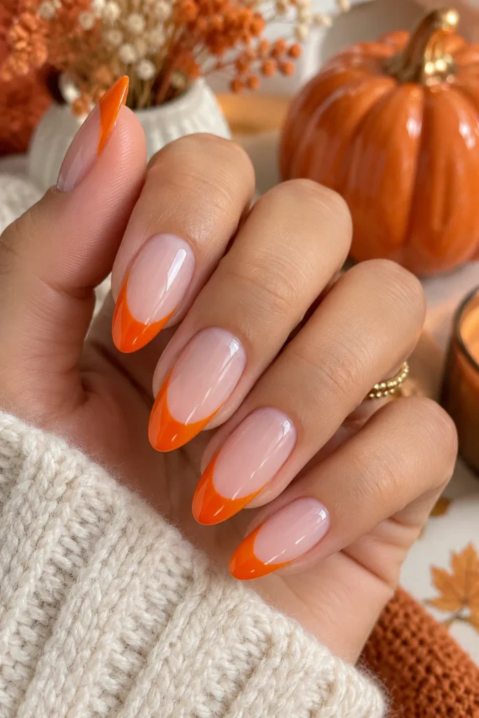 Simple Halloween Almond Nails Design Ideas: Easy Looks features elegant almond nails with vibrant pumpkin-orange French tips, a sheer nude base, a glossy finish, and modern Halloween styling.