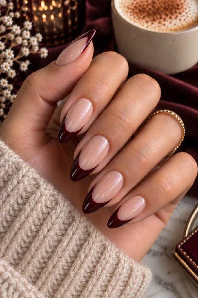 Black cherry and nude French nails with deep wine-colored tips, a sophisticated moody winter autumn manicure in a chic 2026 style.