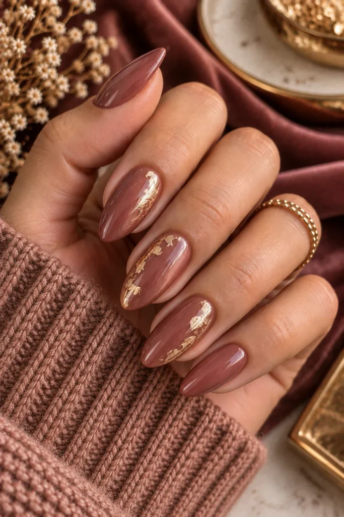 Rosewood nails with delicate gold-leaf accents, a warm, luxurious, minimalist manicure featuring sophisticated winter- and autumn colors for 2026.