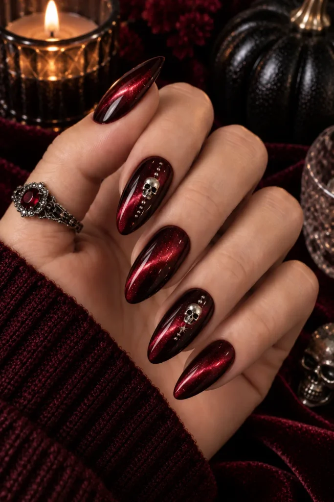 Wine-red cat-eye Halloween nails with luminous magnetic shimmer and tiny metallic skull details in a sophisticated 2026 manicure.