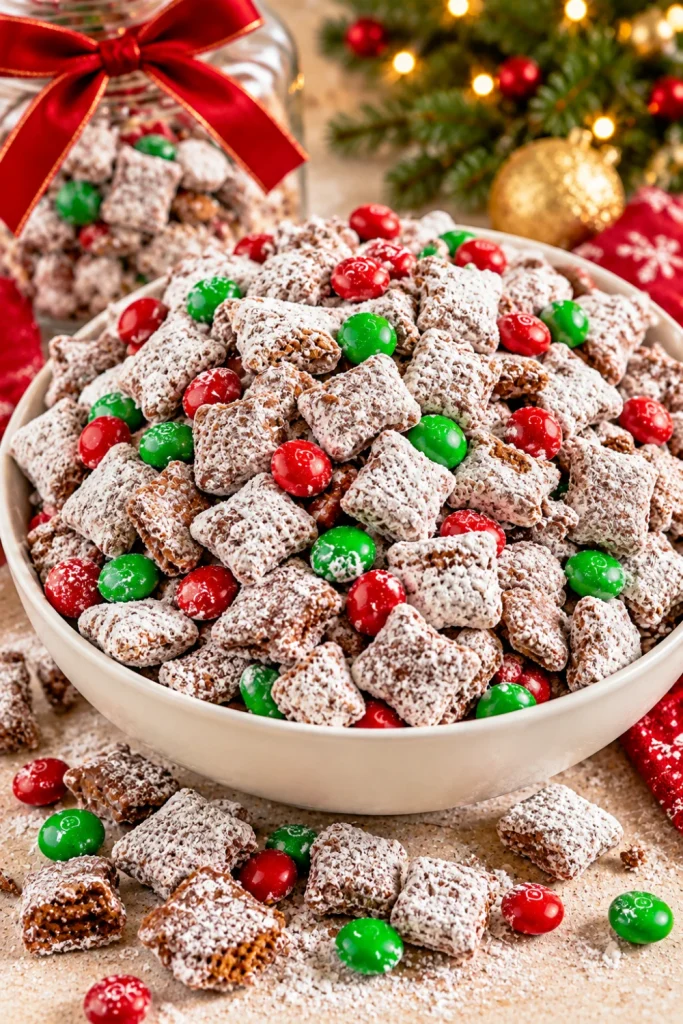 Christmas muddy buddies puppy chow made with chocolate and peanut butter-coated cereal, powdered sugar, and red and green candy-coated chocolates, served as a festive sweet snack for holiday parties and edible gifts.