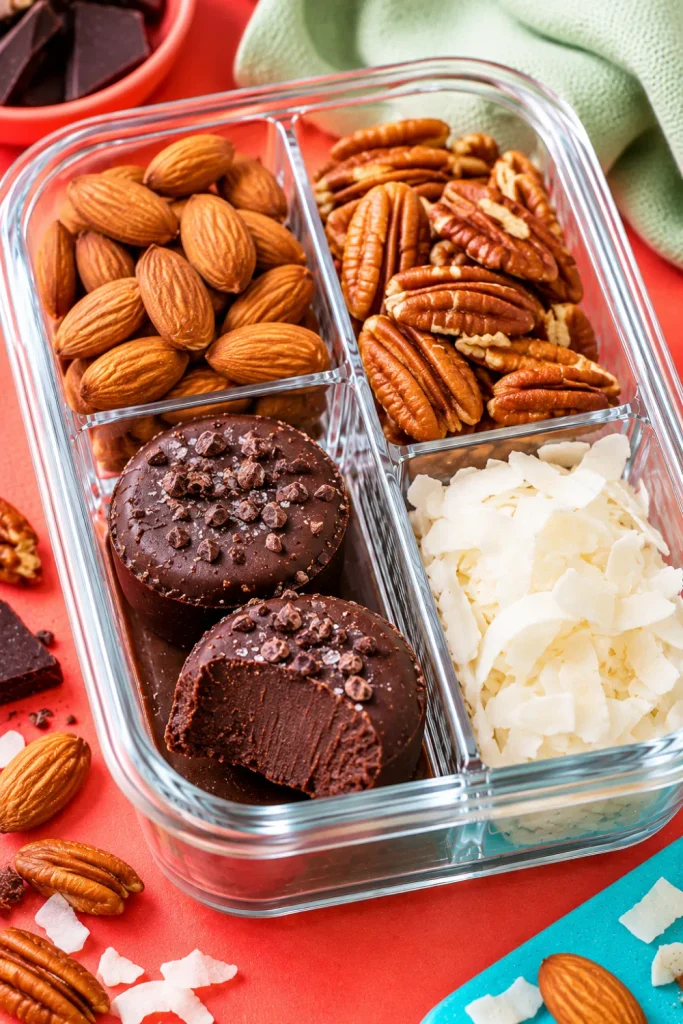 Keto fat bomb and nut snack box with homemade chocolate fat bombs, almonds, pecans, and unsweetened coconut flakes for low-carb meal prep.